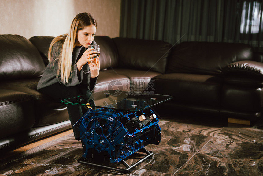 科涅克白兰地威士忌酒年轻的caucasian金发年轻女孩坐在沙地上豪华屋内拿着威士忌杯子特制V8车引擎桌时装照片和美丽的笑容酒鬼图片