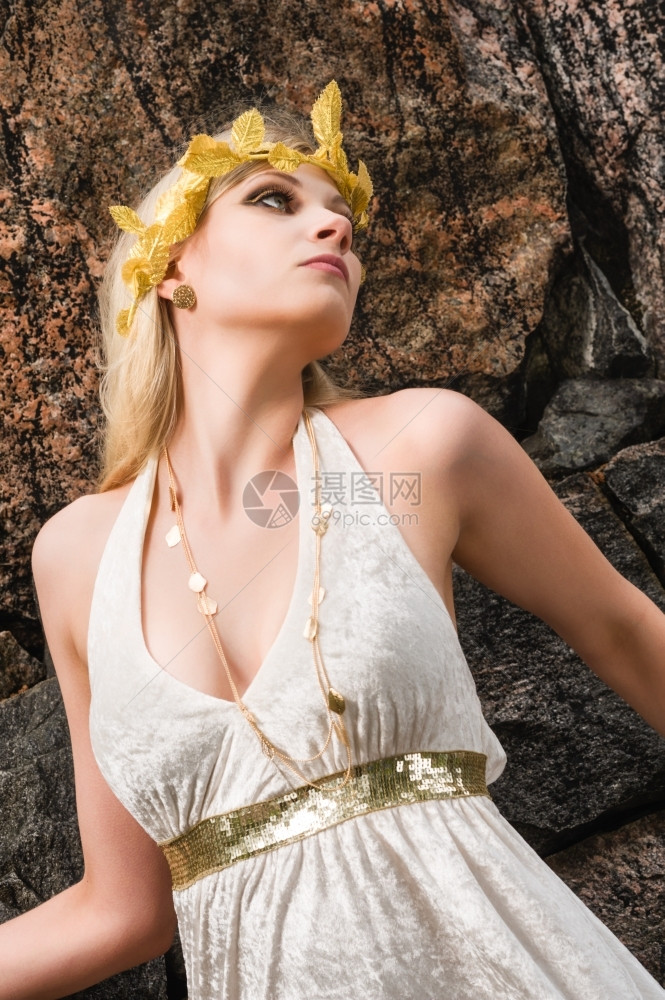 自然妖娆头发美丽的化妆品女孩身着白色外衣和古董珠宝背面有岩石墙图片