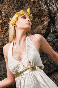 自然妖娆头发美丽的化妆品女孩身着白色外衣和古董珠宝背面有岩石墙图片