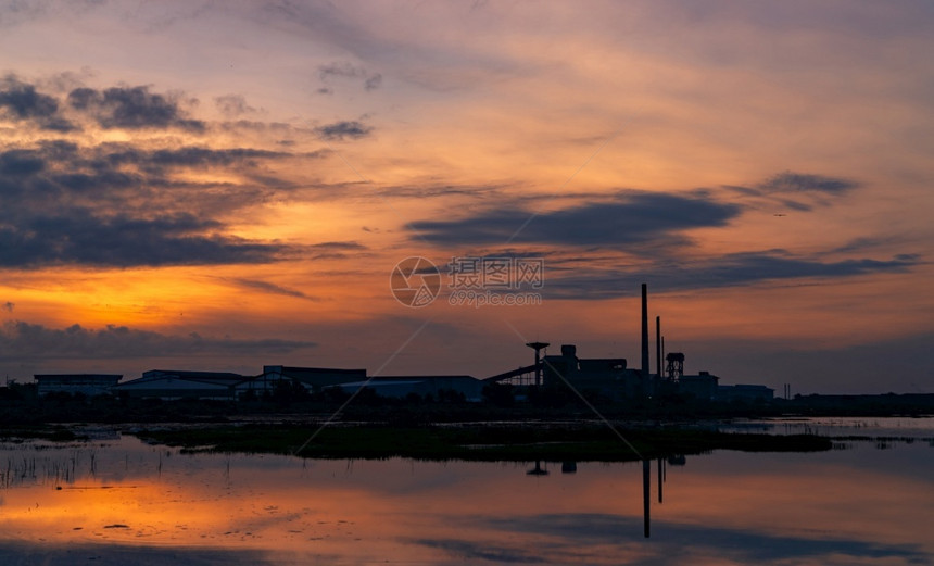 深蓝色和橙黄日落的工厂业建筑风景夜间整洁工厂周围的环境在河仓库大楼水面上反射黑蓝和橙色日落的天空城市黑暗夜晚图片