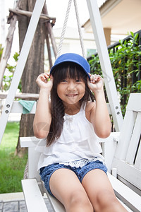 晴天享受坐在摇摆手上的女孩拿着蓝色帽子笑操场图片