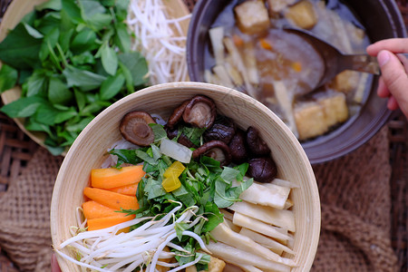 豆腐包子妇女用手从汤锅中勺子准备食物早餐包干草碗竹鱼面和豆腐蘑菇羊叶草药蔬菜的简单但素食可口亚洲越南生的背景