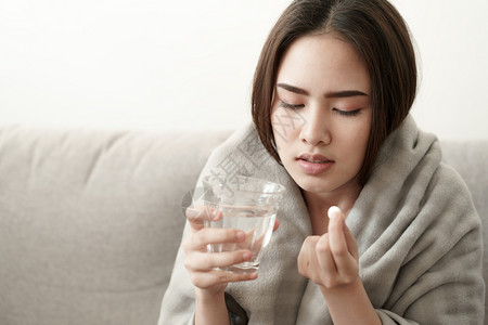 坐在沙发上喝水吃药的女性图片