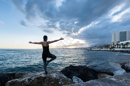 海洋药物女人在阴云的一天海滩上做瑜伽练习年轻的美丽背景