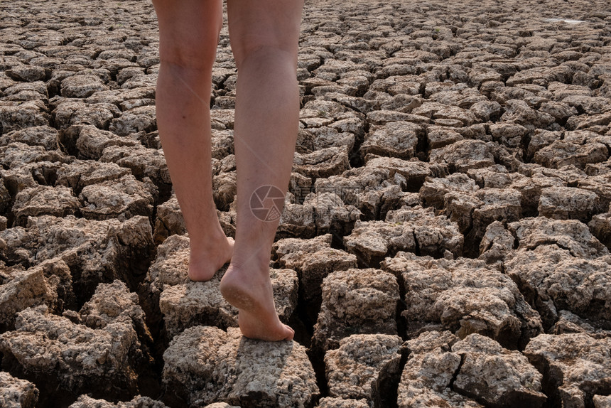 无菌步行人类在干旱地区貌景观干旱危机中行走在破裂和干燥土壤上的妇女图片