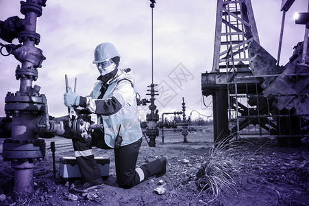 制服矿业机械油气井田修复女工带扳手戴头盔和工作服油井口流程背景