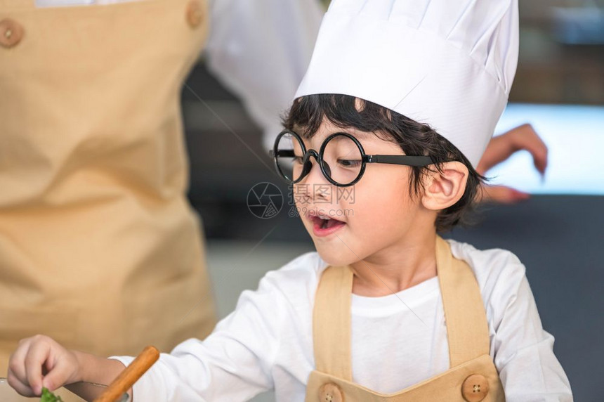 有趣的婴儿微笑穿着大厨帽和围裙的亚洲可爱小男孩与母亲在家中厨房泰国人和生活方式概念工作职业和教育学习概念以及快乐家庭时日主题的关图片