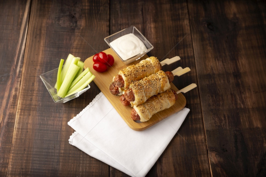 狗扭曲的猪美味香肠零食包在松饼糕里配有芝麻种子加上樱桃西红柿菜棒和酱汁图片