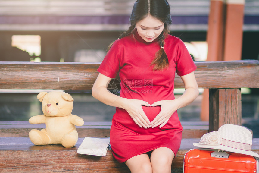 婴儿人们坐在TeddyBear的长椅上在火车站旅行时用红色手提箱绘制ArianRosidProginereddress红裙子亚洲图片