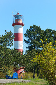 颜色天空灯塔导航天红白塔在树林中站立的红色白灯塔导航和蓝长椅早晨图片