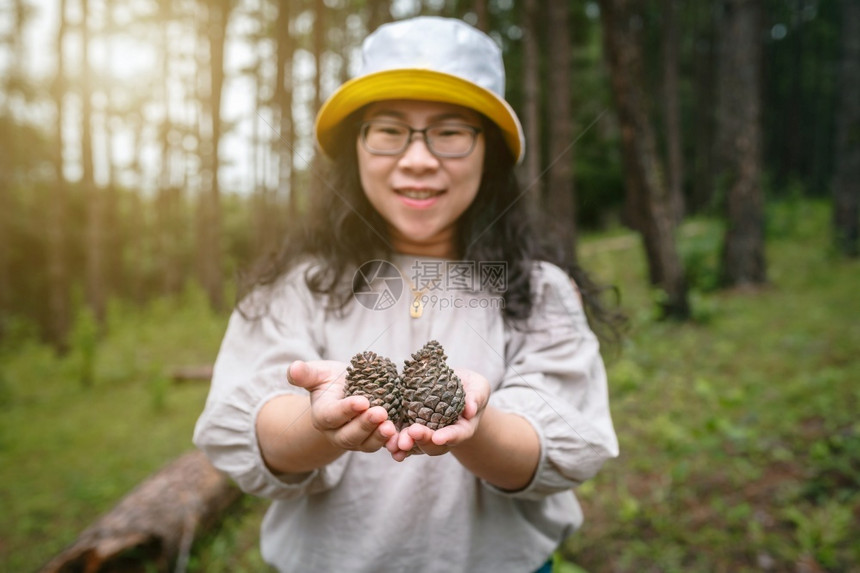 白色的身着礼戴帽子的亚洲女游客在自然小径森林公园上持松树绿中的锥植物群假期图片