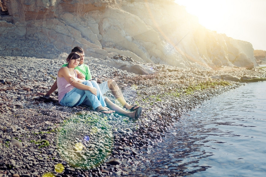 年轻情侣坐在水边仰望阳光照耀女朋友蜜月约会图片