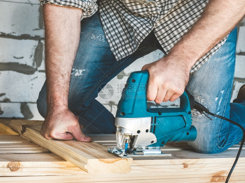 人们穿着棒球帽牛仔裤和衬衫的时装男子用工具在房屋内使用木头工作在建筑中造和修理穿棒球帽牛仔裤和衬衫的时装男子概念家锤图片