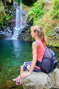 休息马德拉岛的背包作为游客坐在瀑布附近的岩石上荷兰妇女图片