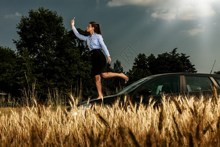 Brunette商业女人在她的汽车上站着时寻找电话信号天空合同专业的图片
