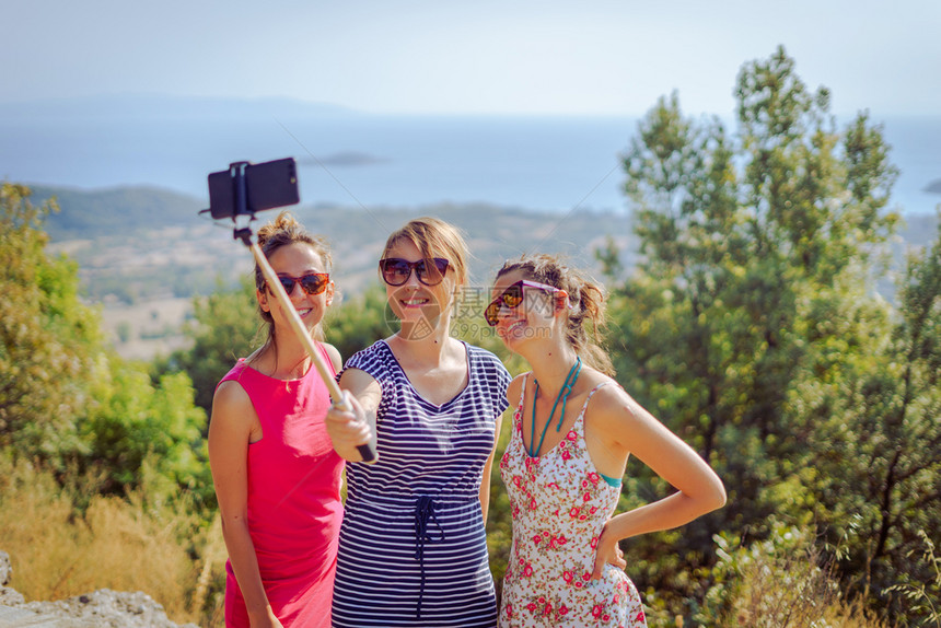 白种人三个穿暑期服装的漂亮女孩旅行者秋天在海上山外用自相棍友情用智能手机拍自乐趣假期图片