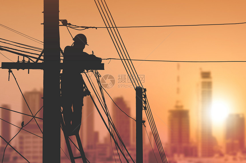 建筑物梯子上的Silhouette电工正在安装缆线路将杆上的互联网信号连接起来在日出天空背景下城市色模糊腰带安全帽图片