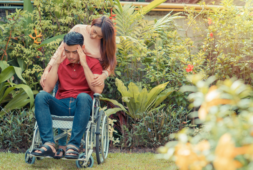 流动失能一位站在轮椅后面的女士正在鼓励她的丈夫脚因意外事故而受伤他的腿因为照顾和支助概念而受伤Africationofcarea图片