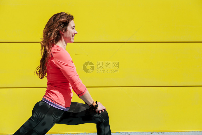 一种年轻姑娘在黄墙前面的地板上伸展然后奔跑健康活力图片