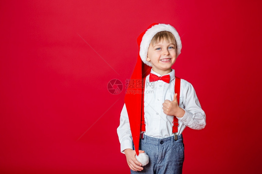 保持可爱的一种圣诞快乐可爱开朗的小男孩戴着红色背景的圣诞老人帽子一个快乐的童年有梦想和礼物图片