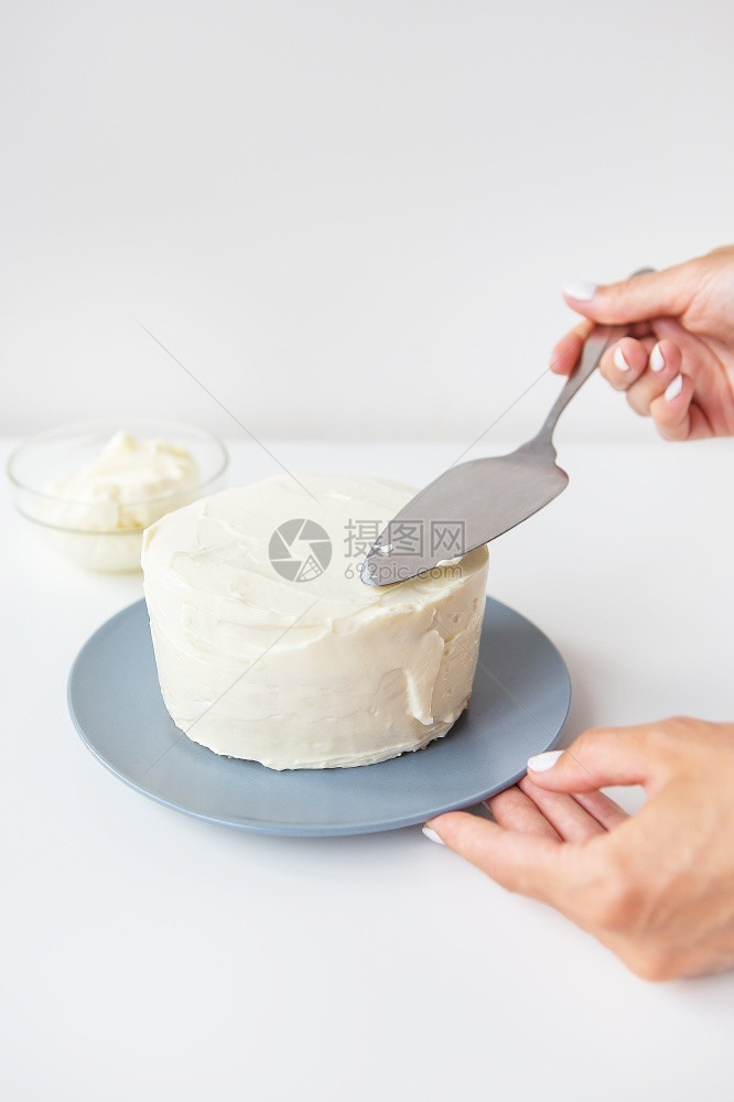 甜点美食味的奶油蛋糕女孩用抹刀涂在生奶油上蛋糕即可装饰美味的奶油蛋糕即可装饰煮熟的图片