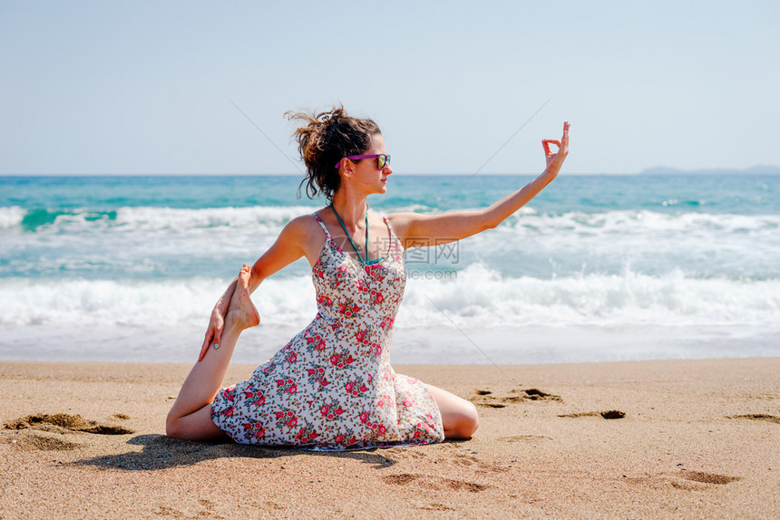 自然冥想夏天穿着衣服的年轻女子在海边滩上练瑜伽在阳光明媚的白天在海边或滨图片