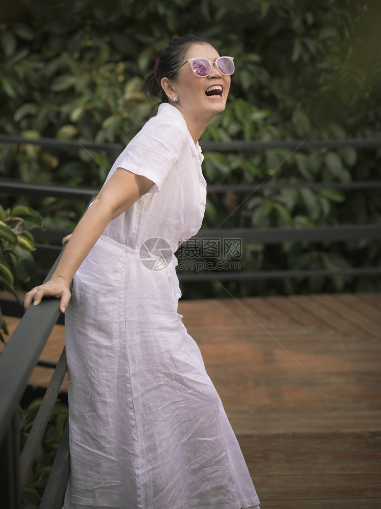 户外幽默妇女穿着白色衣服在绿叶花园中笑着脸面快乐的情绪吸引人图片