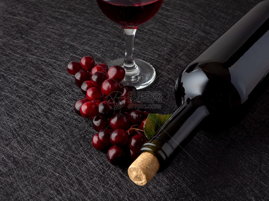 红色的在深背景上躺着一瓶酒和红葡萄在深色背景上躺着一瓶酒和黑葡萄饮料酿酒图片