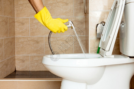 黄色橡胶手套中的人正在用水管喷清洗厕所碗在人们浴室制服图片