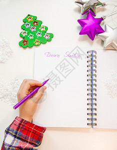 与你童在亲爱的圣诞老人信贺卡孩子左手拿着一支笔左撇子在木制背景的白纸上写字新年装饰童梦想的礼物新年概念孩子拿着笔在他的左手一个撇子在木制设计图片