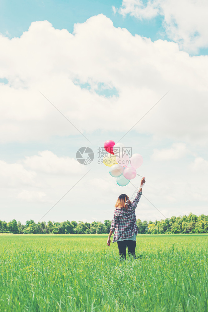 在草原上装有彩色气球的年轻时装女之后是年青时装女在草地上有彩色气球的年轻时装女高阳光头发图片