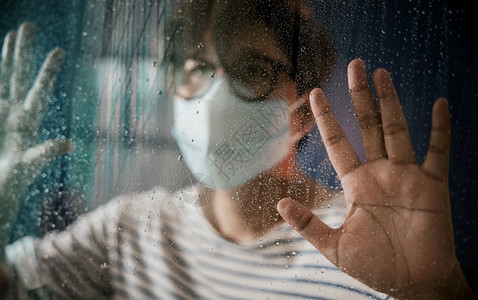 戴着口罩看窗外雨天的男性图片