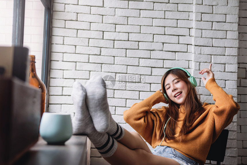 韩国人模型快乐的年轻妇女在CozyHouse从耳机听音乐闭着眼睛和幸福时光中欢快的喜悦时装室内图片
