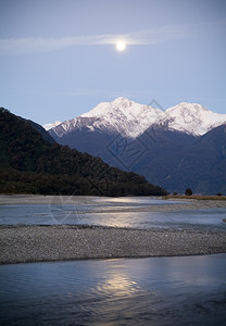 月亮升起于雪盖的山上河流在前方达到高的旅行图片