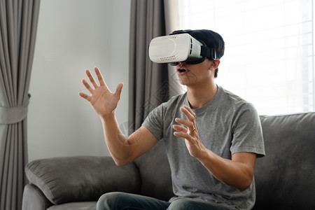 想象一个快乐的男人坐在沙发上戴着3D虚拟真人眼镜乐趣紧张的图片