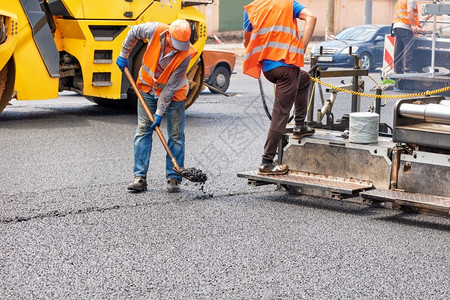 机器建造多层一队道路工人正在沥青摊铺机和压路的帮助下修复一段路在道上铺设一层新的热沥青复制空间一队道路工人正在用业道路机械铺设新背景