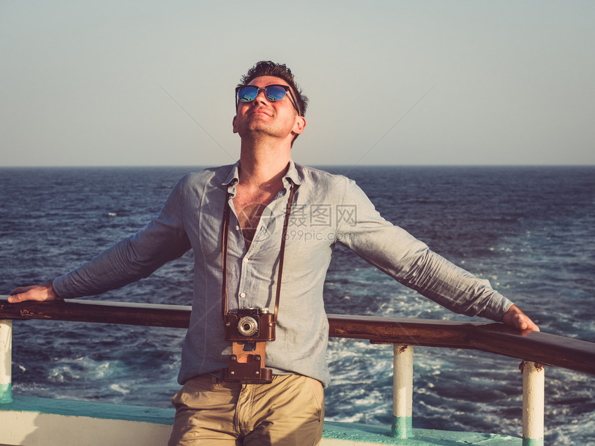 衬垫年轻的商人时装在游轮的空甲板上以海浪为背景在游轮空甲板上持老式照相机的时装人在游轮空甲板上观视特近休闲和旅行概念图片