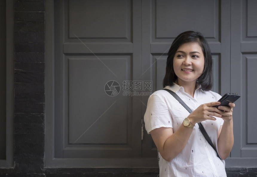 漂亮的视窗年轻有吸引力的亚洲女她们使用智能手机在建筑外黑砖墙上的灰木窗前看侧面用古老的音调风格从事临时形式的亚洲女孩常设图片