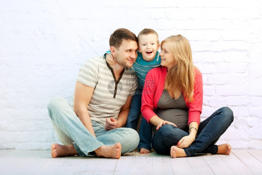 3个幸福的家庭坐在墙旁边的地板上母亲父和小男孩怀孕了她很想知道儿子的情况团体白色的孩子图片