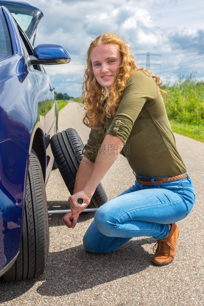 积极的平坦年轻欧洲女在农村公路上换车轮胎技术的图片
