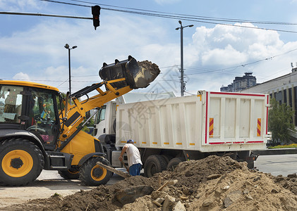 a型一辆橘橙色操纵拖拉机在一辆白色卡车上收集和装载建筑瓦砾A型机动建筑拖拉将堆积瓦砾的装进一辆卡车种可操纵的铺路背景