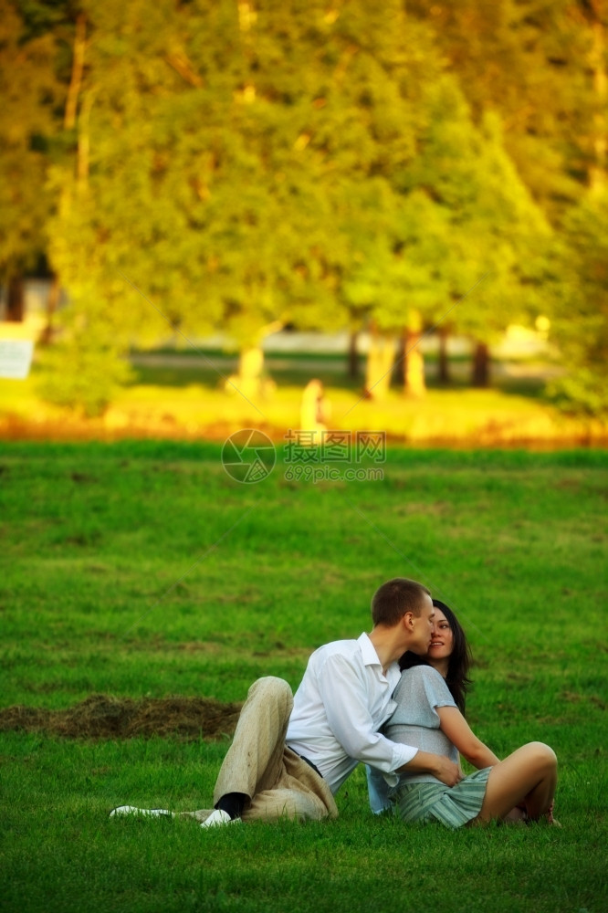 女士喜悦爱的年轻夫妇坐在公园草坪上拥抱图片