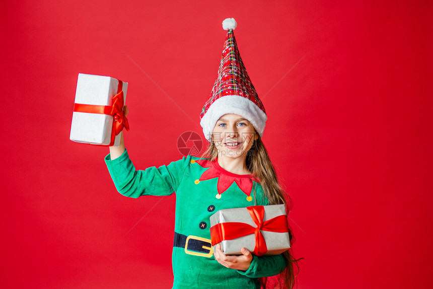 可爱的侏儒游戏圣诞快乐迷人的女孩带着礼物穿鲜艳的红色亮背景上的圣诞老人助手精灵服装一个美丽的精灵婴儿肖像复制空间圣诞快乐带着礼物图片
