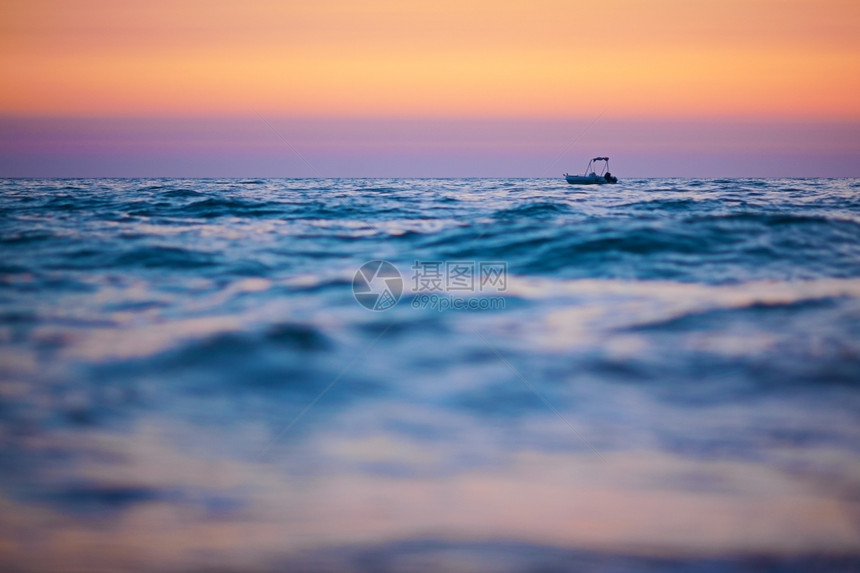 冷静的日落时小船在海浪上航行以船只为重点前景模糊空间复制蓝色的粉图片