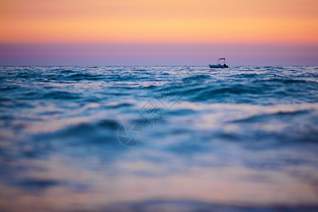 冷静的日落时小船在海浪上航行以船只为重点前景模糊空间复制蓝色的粉图片