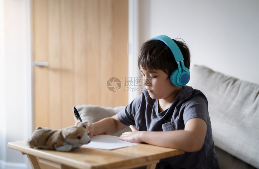 可爱的愉快随意穿着耳机快乐孩子在画纸时聆听音乐室内肖像Cute男孩享受周末在家的创造活动图片