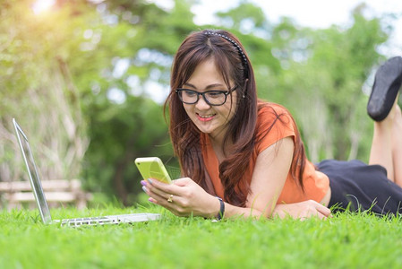 女士铺设亚洲人在公园中放松时使用智能手机的亚洲快乐妇女人与生活方式概念技术和放松主题户外休闲和活动主题笔记本电脑元件计算机背景图片