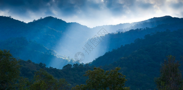 地平线灰蒙绿色戏剧日出闪耀在云中照着山峰和绿林的天空图片