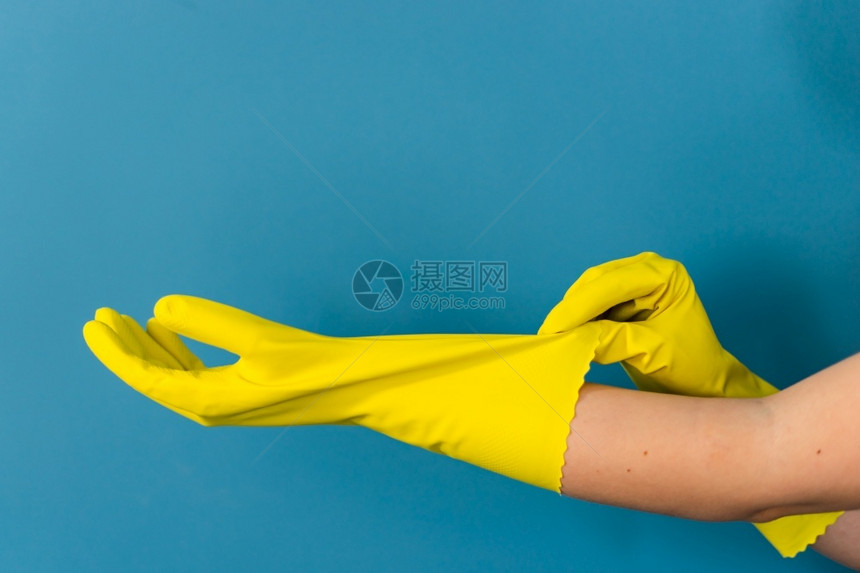 清洁器防水的近距离紧贴着不明的caucasian女孩的手她们要求调整持有保护黄色橡皮手套以便白天对蓝墙背景进行清洁或消毒整理图片