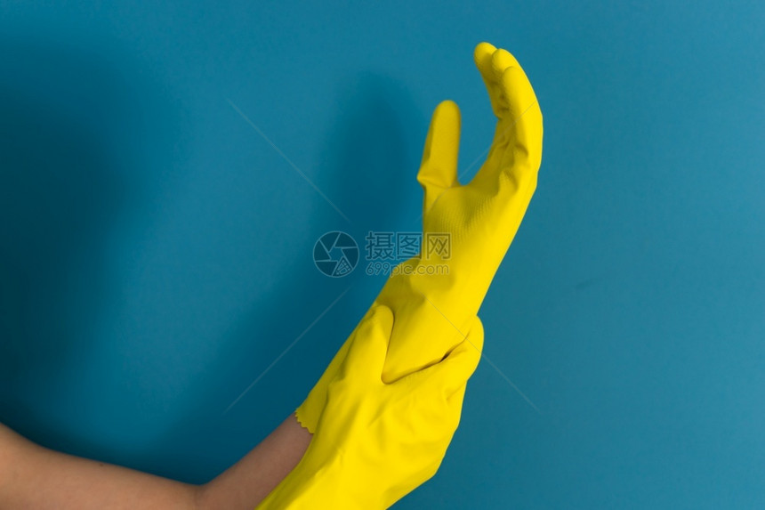 橡胶近距离紧贴着不明的caucasian女孩的手她们要求调整持有保护黄色橡皮手套以便白天对蓝墙背景进行清洁或消毒推杆白种人图片